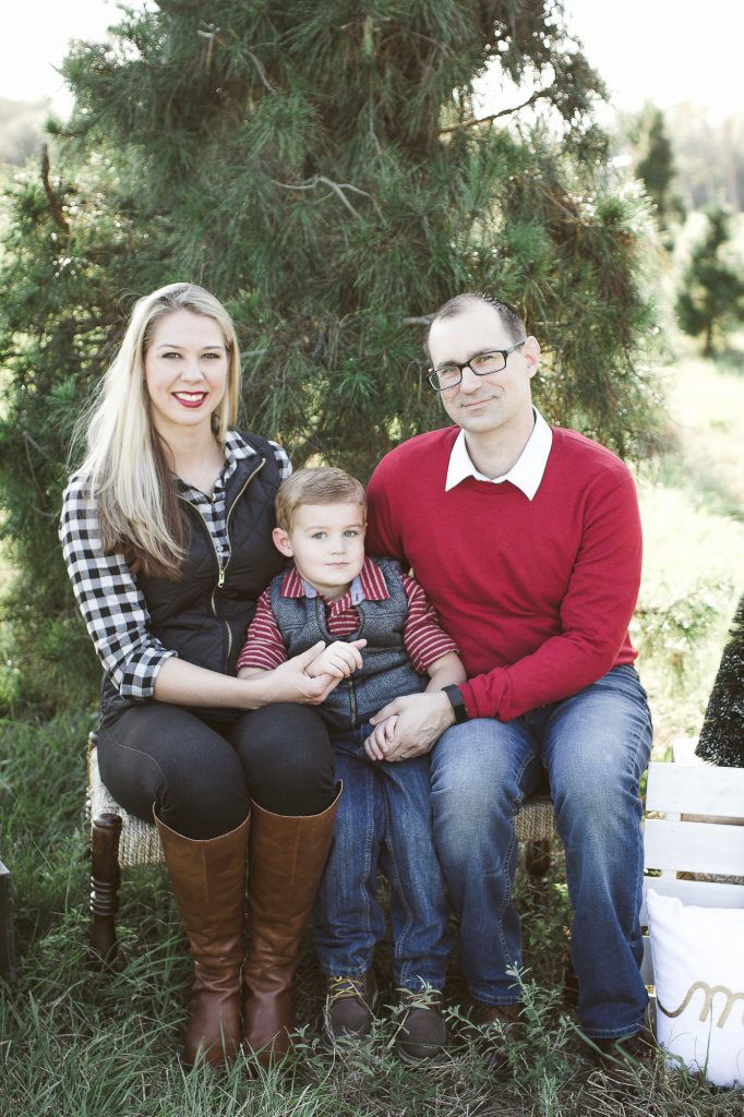A mom, a dad, and their young child sit together on a bench in a natural setting.