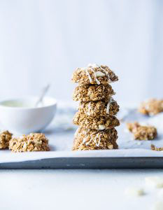 Stack of healthy oat and nut cookies drizzled with white icing, next to a bowl of icing.
